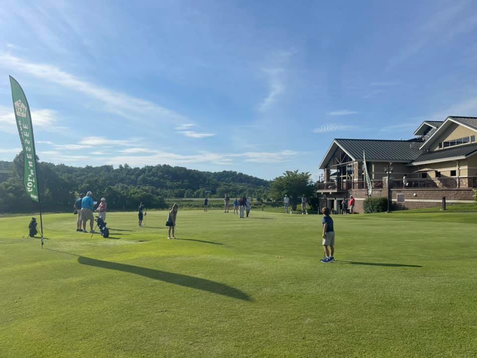 Golfers on golf course during golf event with clubhouse in distance